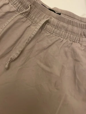 Beige mjukisbyxor med dragsko - Säljer ett par beige mjukisbyxor med avslappnad passform och resår i midjan samt dragsko för justerbar komfort. Byxorna har raka ben och sidofickor. Perfekta för chill dagar eller när du vill vara extra bekväm.
