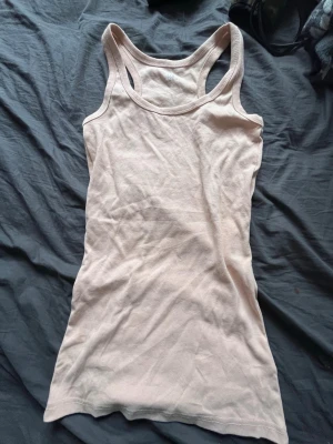 Beige linnetopp från 157 - Säljer en enkel och stilren beige linnetopp från 157 i mjuk ekologisk bomull. Modellen är ärmlös med klassisk racerback och har en tight passform som sitter snyggt på kroppen. Perfekt att matcha med jeans eller shorts.