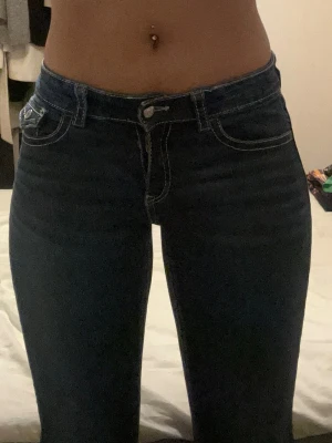 Low waist bootcut jeans från Gina Tricot  - Snygga mörkblå bootcut jeans med vita kontrastsömmar och klassiska fickor både fram och bak. Jeansen har låg midja och är tillverkade i stretchigt denim för en bekväm passform. Perfekta för dig som gillar en tidlös och trendig look. Från Young linjen på Gina Tricot.