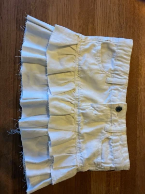 Vit volangkjol med fickor - Kort vit kjol med dubbla volanglager och råa kanter. Kjolen har fickor fram och bak, bälteshällor  