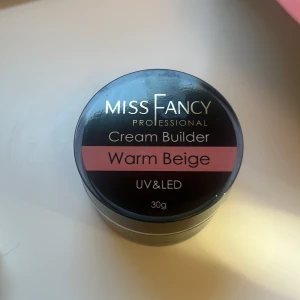 Miss Fancy Cream Builder Warm Beige - Bygggel för naglar från Miss Fancy i färgen Warm Beige. Gelen har en krämig konsistens och passar för både UV- och LED-lampa. Perfekt för att skapa naturliga och snygga naglar med en varm beige ton. Innehåller 30g.