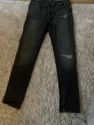 Svarta slitna jeans  - Säljer ett par svarta jeans med raka ben och slitningar på både lår och knä. Jeansen har klassisk femficksmodell och detaljerade slitningar för en trendig look. Perfekta för dig som gillar en avslappnad och edgy stil.