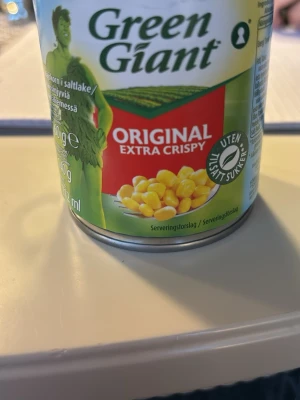 Green Giant majsburk original - En burk Green Giant Original Extra Crispy majs utan tillsatt socker. Burken har grön och gul design med en illustration av majs och en grön figur på framsidan. Perfekt till matlagning eller som tillbehör.