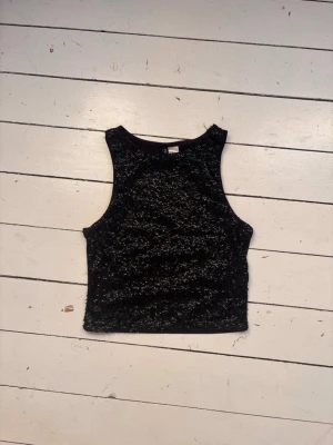 Svart glittrig croppad linnetopp, fest! - Snygg svart croppad linnetopp med glittriga paljetter på framsidan. Ärmlös modell med rund halsringning och tight passform. Perfekt för dig som vill sticka ut lite extra.