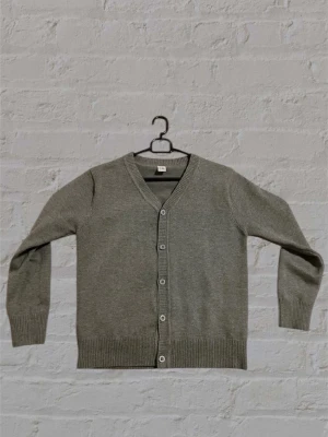 Grå basic kofta med knappar - En stilren grå kofta med v-ringning och knäppning framtill. Koftan har långa ärmar, ribbade muddar och nederkant. Perfekt att slänga över en t-shirt för en enkel och clean look.