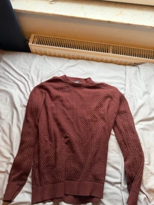 Brun stickad tröja med strukturmönster - Säljer en brun stickad tröja med snygg struktur i materialet. Tröjan har rund halsringning, långa ärmar och breda ribbade muddar vid ärmslut och nederkant. Perfekt för dig som gillar en enkel men ändå stilren look.