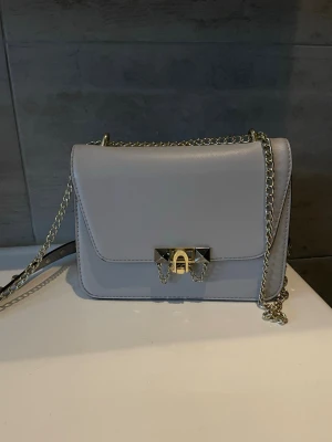 Ljusgrå väska med guld detaljer  - Säljer den här snygga handväskan med gulddetaljer  Kommer tyvärr inte till användning  Älskar färgen och älskar de små guld detaljerna, speciellt på axelbandet där de sitter som små nitar Fint skick, som på alla bilder