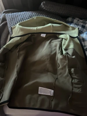 Olivgrön hoodie från Nike - Säljer en olivgrön hoodie från Nike med dragkedja och huva. Hoodien har svarta detaljer längs kanterna och är tillverkad i ett mjukt och bekvämt material. Perfekt för dig som gillar en sportig och avslappnad stil.