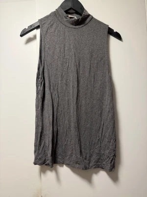 Grå ärmlös polotopp från H&M - Snygg grå ärmlös polotopp från H&M i mjuk bomullsblandning. Perfekt att styla med jeans eller kjol för en clean och enkel look. Polokrage och rak passform ger en modern vibe.