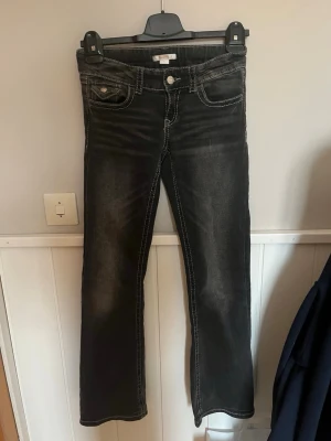 Svarta bootcut jeans från Gina Tricot - Snygga svarta bootcut jeans från Gina Tricot med markerade vita sömmar och klassisk femficksdesign. Jeansen har en lätt tvättad look och är perfekta för dig som gillar en trendig och avslappnad stil.