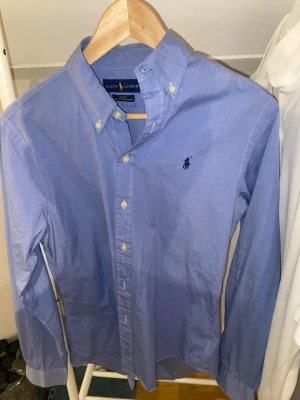 Blå skjorta från Ralph Lauren - Jag säljer en blå Ralph Lauren skjorta i perfekt skick, den är slim fit i storlek M. Säljer på grund av att den är för liten tyvärr men man ser inga tecken på användning. Hör av er vid prisförslag!