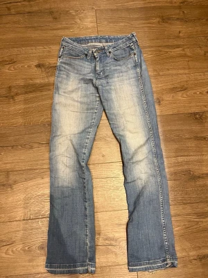 Blå bootcut jeans med slitningar - Snygga blå bootcut jeans med ljusa slitningar framtill och klassisk femficksdesign. Jeansen har normal midja och dragkedja med knapp. Perfekta för en avslappnad och trendig look.