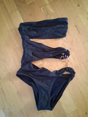 Svart bikini med flätade detaljer - Snygg svart bikini med bandeau-topp och matchande trosa. Båda delarna har flätade detaljer i sidorna som ger en unik look. Perfekt för stranden eller poolen. Enkel och stilren design som passar till det mesta.