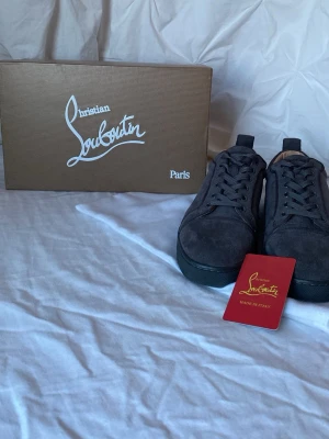 Mörkgrå mocka sneakers Louboutin - Snygga mörkgrå sneakers från Christian Louboutin i mjuk mocka med klassisk röd sula och snörning. Skorna har en stilren och modern design som passar perfekt till streetwear och modeintresserade. Kommer med originalkartong och dustbag. vet ej om det är äkta men det ser väldigt äkta ut från mitt perspektiv.