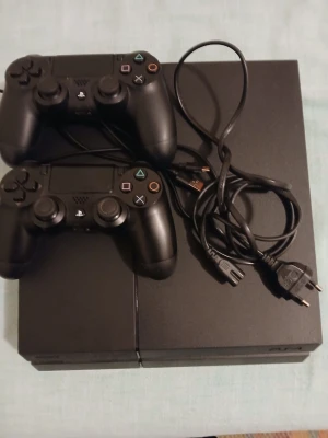 PlayStation 4 med två handkontroller - Säljer en svart PlayStation 4 från Sony med två matchande DualShock 4-handkontroller och strömkabel och en laddare. Konsolen har en stilren, rektangulär design i matt och blank plast. Perfekt för gamingkvällar och multiplayer med vänner. 