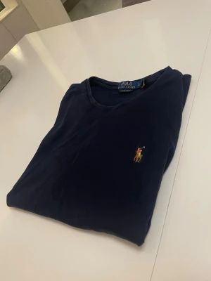 Ralph Lauren t shirt  - Klassisk mörkblå t-shirt från Ralph Lauren med den ikoniska broderade loggan på bröstet. T-shirten har rund halsringning och korta ärmar. Tillverkad i mjuk bomull för en skön känsla och clean look.