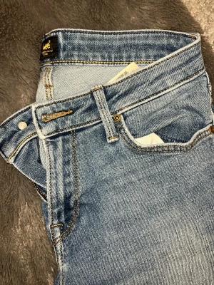 Blå raka jeans från Lee - Klassiska blå jeans från Lee med raka ben och fem fickor. Jeansen har tydliga kontrastsömmar och Lee-logga på bakfickan. Storlek S och sitter väldigt skönt!