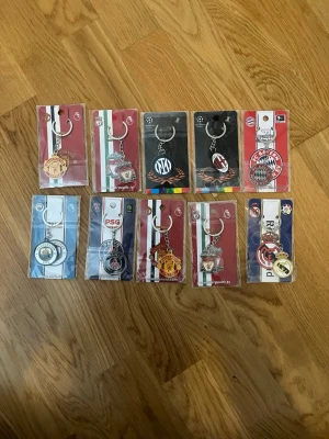 Samling fotbollsnyckelringar - Säljer en samling med tio olika fotbollsnyckelringar från kända europeiska klubbar. Nyckelringarna är i metall och plast, med klubbarnas logotyper i färger som röd, blå, svart och vit. Perfekt för dig som älskar fotboll och vill visa ditt favoritlag på väskan eller nyckelknippan 99 kr styck .