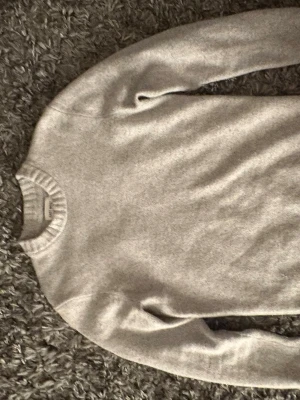 Grå stickad tröja från EAST WEST - En stilren grå stickad tröja med rund halsringning och ribbade muddar vid ärmslut och nederkant. Perfekt för sena sommarkvällar,vår, vinter och enkel att matcha med olika outfits. Mjuk och skön känsla.