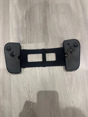 Svart Ipad handkontroll  - Säljer en svart Ipad handkontroll. Den har två analoga spakar, styrkors, och klassiska ABXY-knappar. Kontrollen är gjord i plast och har en flexibel design som passar runt Ipaden för gaming on-the-go. 