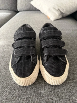 Even&Odd skor i storlek 38 - Snygga svarta sneakers i manchestertyg med tre breda kardborreband och vit sula. Skorna har en klassisk låg modell och passar perfekt till streetwear-stilen. Bekväma och lätta att ta på tack vare kardborreknäppningen.