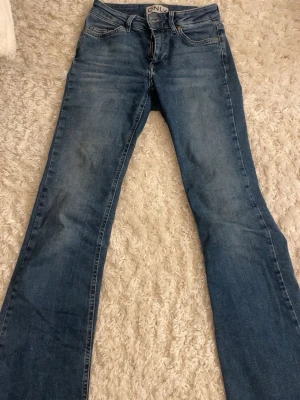 Blå bootcut jeans från ONLY - Säljer ett par klassiska blå bootcut jeans från ONLY. Jeansen har fem fickor, normal midja och snygga slitningar framtill. Tillverkade i mjuk denim med lite stretch för extra komfort. Perfekta till sneakers eller boots för en avslappnad look.