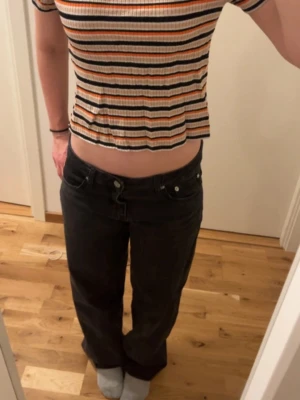 Randig croppad topp med fina färger  - Säljer en croppad ribbad topp med korta ärmar och rund hals. Toppen har ett färgglatt randigt mönster i orange, svart, vit och beige. Perfekt för dig som gillar en avslappnad och trendig stil. Står M på lappen men skulle påstå mer en S. 