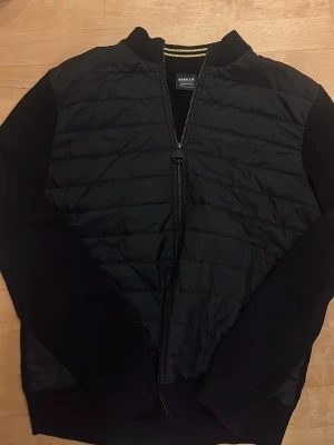 Barbour jacka  - Säljer nu min jacka från Barbour. Den är i riktigt bra skick. Jackan har dragkedja framtill, ribbade muddar och klassisk bomberkrage. Perfekt för dig som vill ha en stilren och modern look.