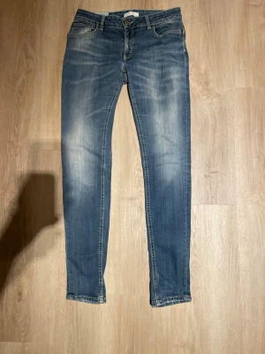 Blå slim fit jeans med slitningar - Snygga dondup blå slim fit jeans med lätt slitna detaljer. Jeansen har en något tvättad look och raka ben. Perfekta för en avslappnad och trendig stil. Materialet är denim i bomull.