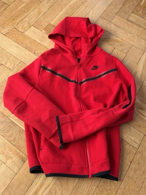 Röd nike tech - Riktigt snygg röd zip-hoodie ifrån Nike. Jag kommer fixa till armarna så att de inte är vikta innan jag skickar tröjan så den ser nyare ut.  