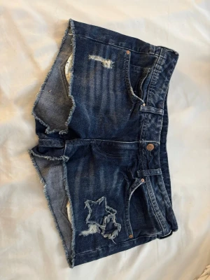 Mörkblå jeansshorts med slitningar - Snygga mörkblå jeansshorts med råa kanter och slitningar, inklusive en stjärnformad reva på ena benet. 💕 perfekt för sommar, storlek 38 men passar mig som har 34