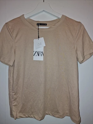 Beige t-shirt från Zara - Snygg beige t-shirt som passar till jeans, under koftan/kavajen och är perfekt som basplagg i garderoben.