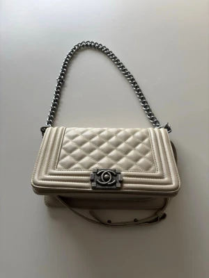 Snygg beige handväska  - Säljer en snygg begie handväska i  läder med silverfärgad kedjerem och ikoniskt CC-spänne framtill. Väskan har en stilren, rektangulär form och justerbar axelrem. Perfekt för dig som vill ha en klassisk och trendig handväska från ett lyxigt märke.