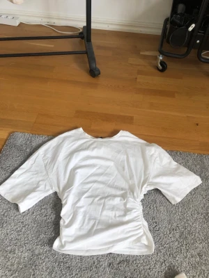 Vit croppad t-shirt Gina Tricot - Säljer en vit croppad t-shirt från Gina Tricot i storlek XS. T-shirten har korta ärmar och en snygg rynkad detalj i sidan som ger en trendig look. Perfekt till jeans eller kjol för en enkel men stylish outfit.