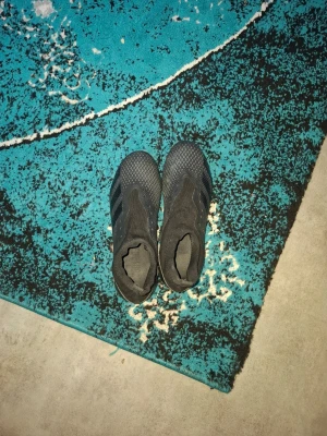 Svarta adidas fotbollsskor utan snörning - Säljer ett par svarta fotbollsskor från adidas med klassiska tre ränder på sidan. Skorna har en strumpliknande passform utan snörning och ovandel i textil och syntetmaterial för bra bollkontroll. Perfekta för dig som vill ha stilrena och funktionella skor på planen.