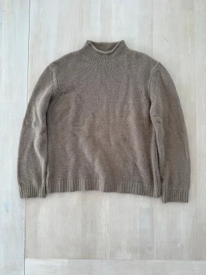 Beige stickad tröja med polokrage - En enkel och stilren beige stickad tröja med polokrage i kashmir och ylle. Tröjan har långa ärmar och ribbade muddar vid ärmslut och nederkant. 