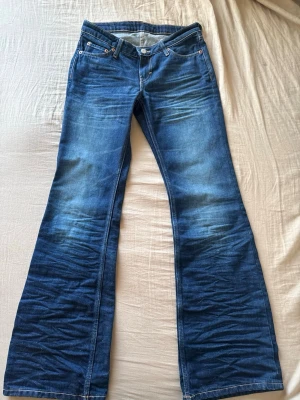 Blå bootcut jeans från Weekday - Säljer ett par snygga Weekday Nova Low Bootcut Wrinkle Jeans i mörkblå tvätt. Låg midja med bootcut-modell som är smal över låren och svänger ut nedtill. Jeansen har en trendig, förtvättad look med markerade slit- och veckdetaljer framtill och längs benen.