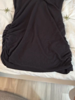 Svart linne med rynkade sidor - Säljer ett svart linne med snygga rynkade detaljer på sidorna. Linnet har en enkel och stilren design som passar perfekt till många olika tillfällen. Materialet känns mjukt och följsamt mot kroppen.