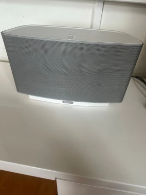 Sonos Play:5 trådlös högtalare vit gen 1  - Snygg och kraftfull Sonos Play:5 trådlös högtalare i vit och grå design. Högtalaren har en stilren, rektangulär form med metallgaller framtill och plastchassi. Perfekt för att streama musik trådlöst med riktigt bra ljudkvalitet. Har 2 st och den här har bara används ngr ggr pga placering 