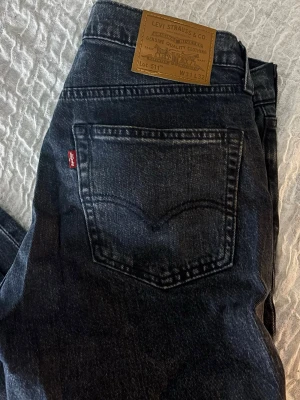 Levi's 511 svarta jeans W31 L32 - Säljer ett par svarta Levi's 511 jeans med klassisk femficksdesign och dragkedjegylf i storlek W31 L32. Jeansen har en snygg tvättad look. 