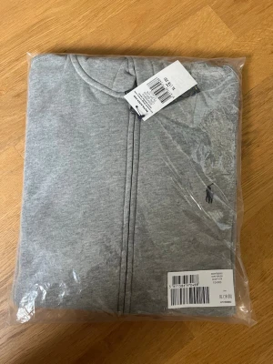 Grå hoodie från Ralph Lauren Storlek Small  - Säljer en snygg grå hoodie från Polo Ralph Lauren. Storlek XL (Barn) och det motsvarar storlek XS-S i Herr storlek.                                            Hoodien har dragkedja framtill, huva med justerbara snören och den ikoniska Ralph Lauren-loggan broderad på bröstet. Tillverkad i mjuk och bekväm bomullsblandning som passar perfekt för både vardag och avslappnade outfits. Den är helt ny och paketet har aldrig öppnats. ✅