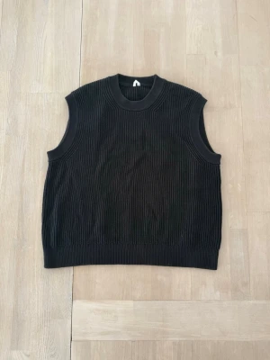 Blå ribbad stickad väst - Stilren blå stickad väst med ribbad struktur och rund hals. Perfekt att bära över en skjorta eller t-shirt.