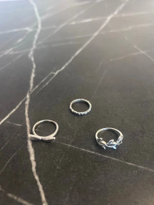 Tre silvriga ringar i olika designer - Säljer tre stilrena silvriga ringar. En har tvinnad design, en är dekorerad med små pärlor runt om och en har ett lövmönster. Perfekta att mixa och matcha för en personlig stil.