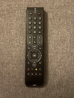 Svart universalfjärrkontroll - En svart universalfjärrkontroll från One For All med många knappar för olika funktioner, inklusive volym, kanalval, guide och färgknappar. Passar till flera olika TV-modeller och har en klassisk avlång form i plast.