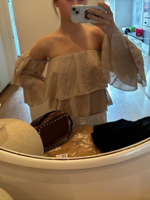 Beige offshoulder volangblus - Trendig beige offshoulder blus med dubbla volanger och vida ärmar. Luftigt material som ger en bohemisk känsla och passar perfekt till sommaren. Snygg att styla med både jeans och kjol.