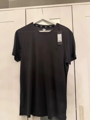Mörkgrå tränings t-shirt från 157 - En helt ny mörkgrå tränings t-shirt från 157 med rund hals och korta ärmar. Helt ny med prislapp kvar. Tillverkad i ett lätt och mjukt material som känns skönt mot huden. Perfekt till jeans eller shorts för en enkel och clean look.