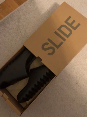 Svarta Yeezy Slide tofflor - Yeezy Slides är något mindre i passformen än vanliga tofflor. skulle därför rekommendera storlek 44 till dig som normalt har storlek 43 med smalare fötter, eller storlek 42 med bredare fötter.  Skicket är nästan som nytt – de har endast använts vid ett fåtal tillfällen och har inga större tecken på användning. 