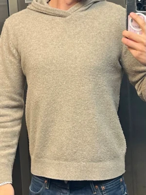 Beige Merino ull tröja - En stilren beige stickad tröja med rund hals och långa ärmar. Tröjan har ribbade muddar vid ärmslut och nederkant, vilket ger en snygg och klassisk look. Perfekt att matcha med jeans för en enkel och avslappnad stil.