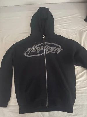 Svart zipup y2k style - Svart hoodie med hel dragkedja och huva. Framsidan har ett stort, diamant grafiskt tryck över bröstet och dragkedjan har en stjärnformad detalj upptill. Hoodien har långa ärmar och en avslappnad passform, perfekt för en streetwear-look. Från newyorker