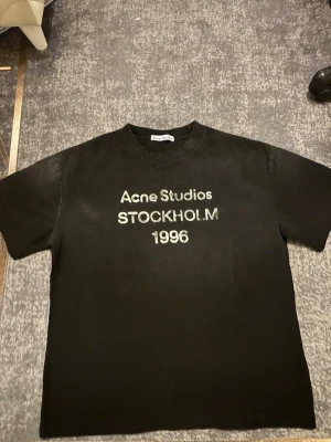 Svart Acne Studios t-shirt - En svart t-shirt från Acne Studios med tryck i vitt framtill där det står 'Acne Studios STOCKHOLM 1996'. Klassisk rund hals och korta ärmar. 
